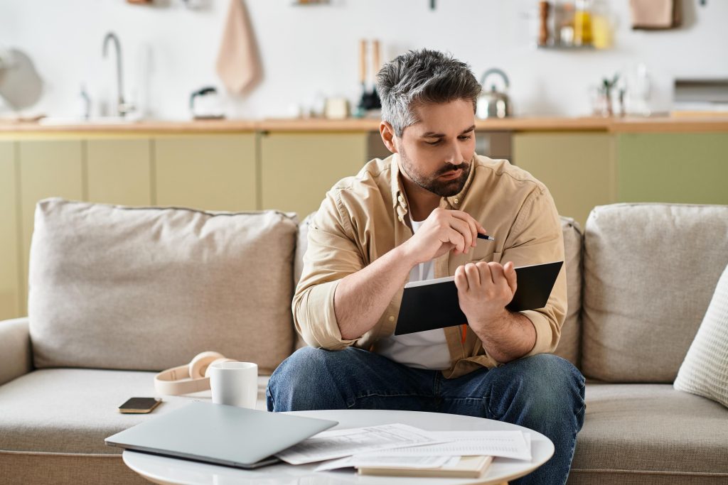 A man writing notes at a desk in a living room.