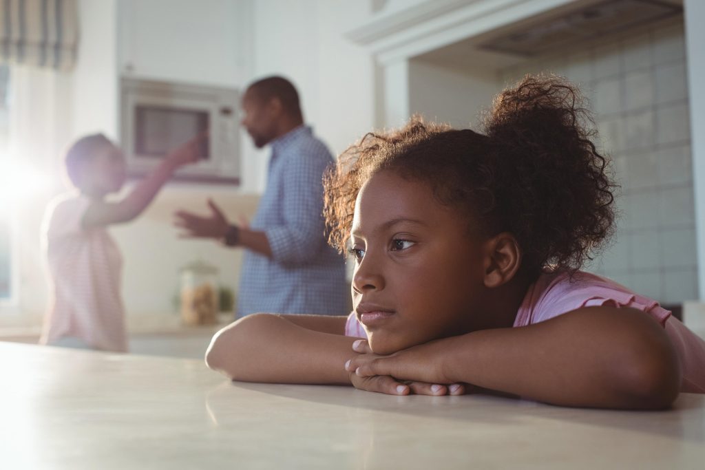 A child sitting in a kitchen while her parents talk.