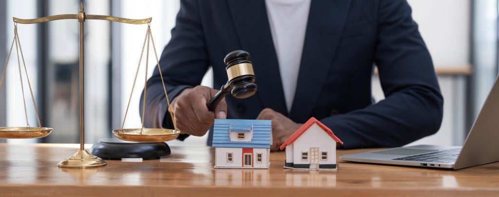 Close-up of a house in front of a lawyer holding a hammer and a laptop silver brass scales on a wooden table in his office, law, legal services, advice, justice and real estate ideas.