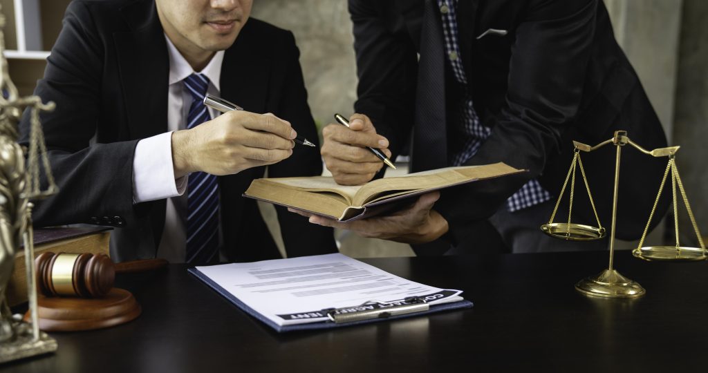 Two people in suits are examining a document and an open book at a desk.