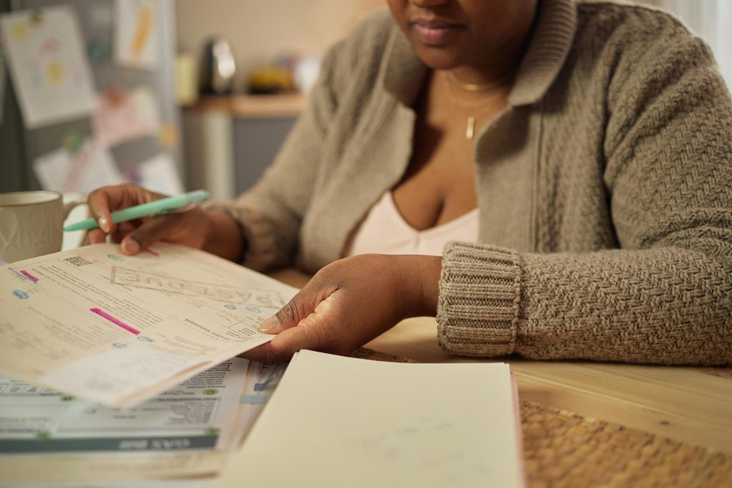 Close up of Black middle aged woman reviewing bills and paperwork at home, managing household budget and financial stress. Useful for poverty, debt, cost of living, assistance campaigns