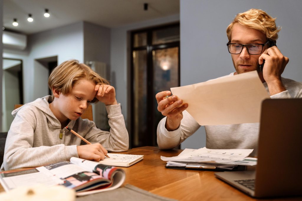 Ginger son doing homework while his father talking on cellphone at home