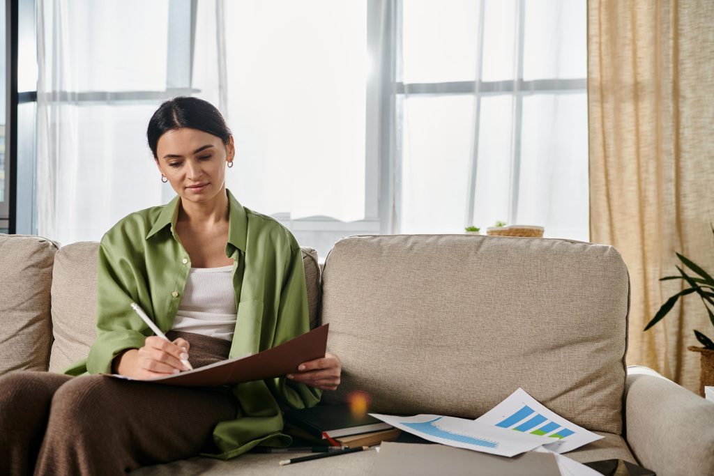 Woman in casual attire sitting on couch, holding pen and paper.