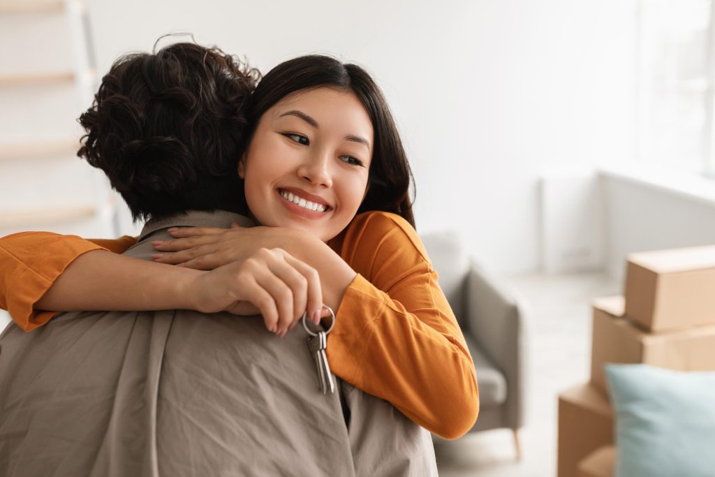 Smiling young Asian woman hugging her boyfriend and holding house key on moving day, free space