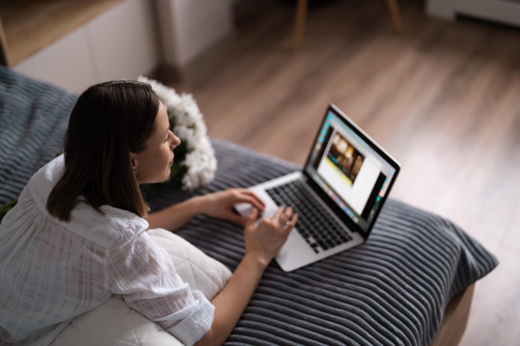 Woman communicating using a laptop while stating on bet with a bunch of white flowers
