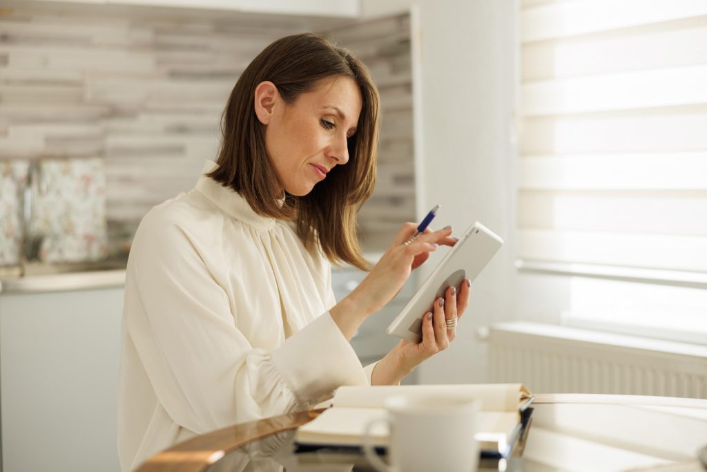 Woman writing notes in planner and using tablet computer while w